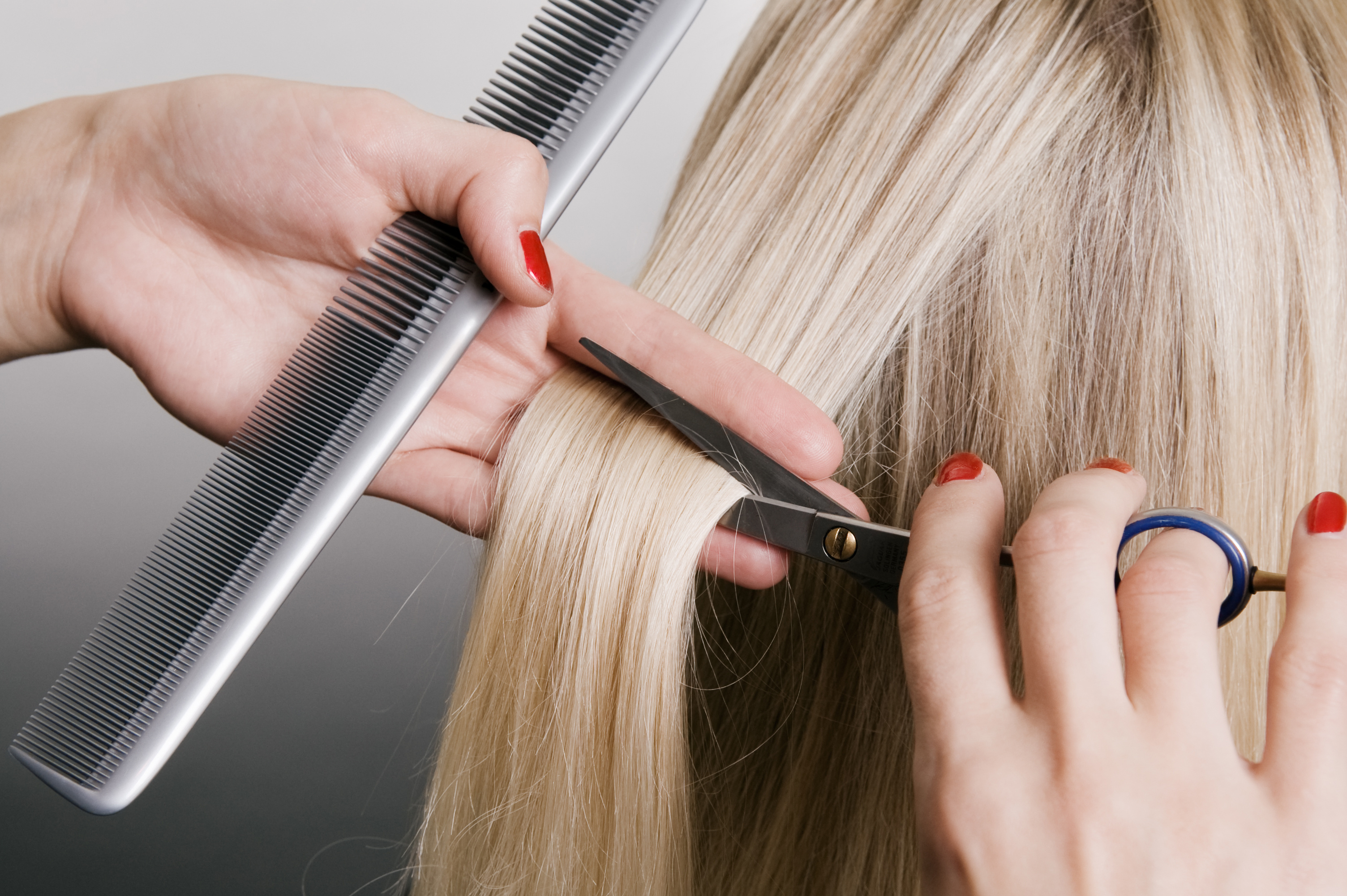 Hairdresser Cutting Blonde Hair Closeup Over Grey Background